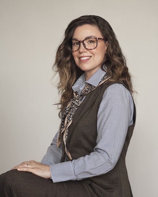 Profile of woman with glasses, long brown hair, and professional attire.