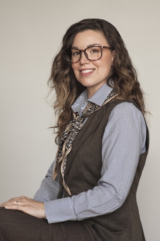 Profile of woman with glasses, long brown hair, and professional attire.